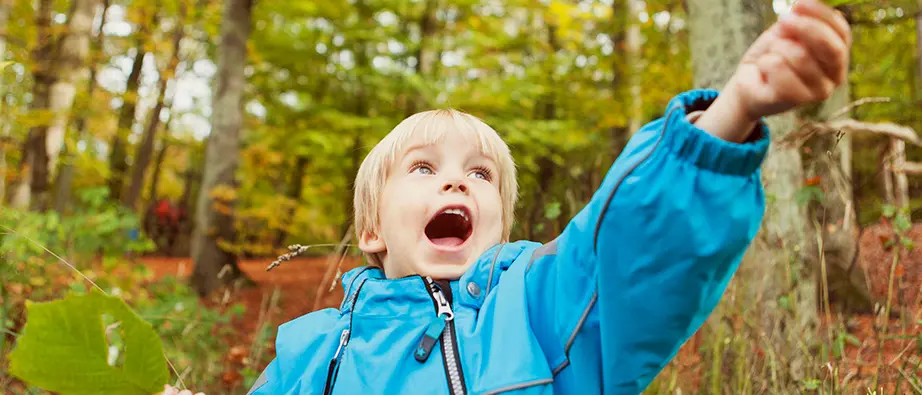 Ett barn som är glad och sträcker ut handen med ett löv i handen.