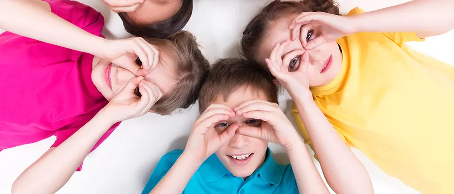 Barn i färgglada t-shirts håller händerna som en kikare framför ögonen och ser glada ut.