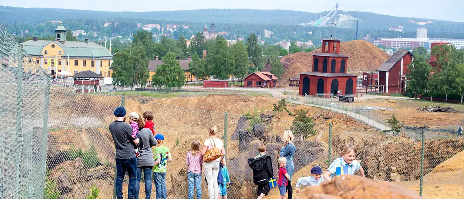 En grupp människor står och tittar ut över gruvhålet i Falun. I bakgrunden syns Falu stad och skidhoppbackarna. 
