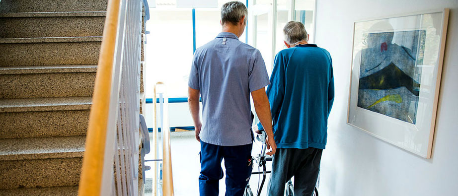 Skötare med äldre går bredvid varandra
