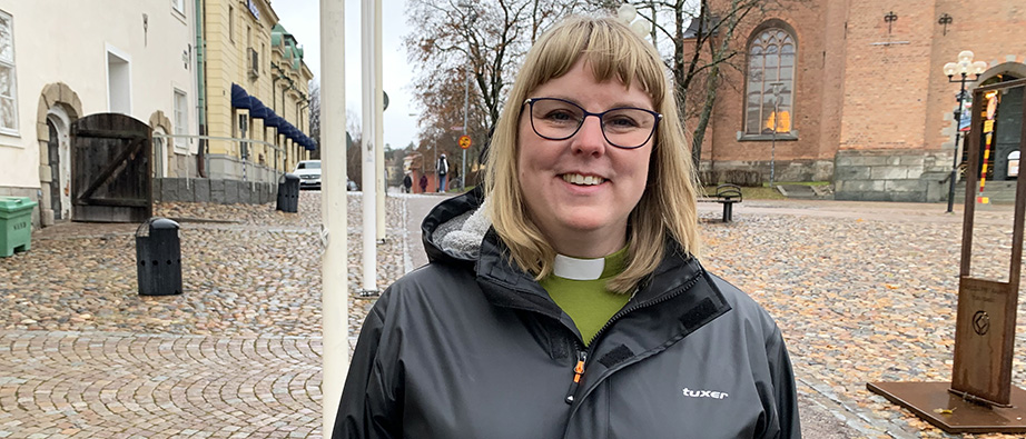 Emelie Kjellgren står på Stora torget i Falun. Bakom syns Kristine kyrka. Emlie har glasögon, blont hår och har en regnkappa på sig.