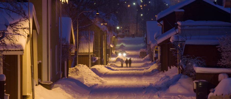 Bild på lång gata med snö och faluröda hus på vardera sida.