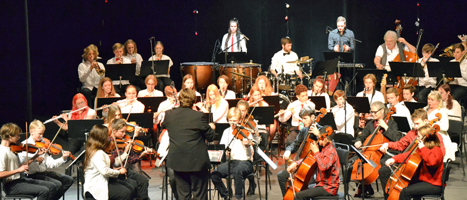 Stor orkester, många musikanter på en scen och en dirigent står framför orkestern