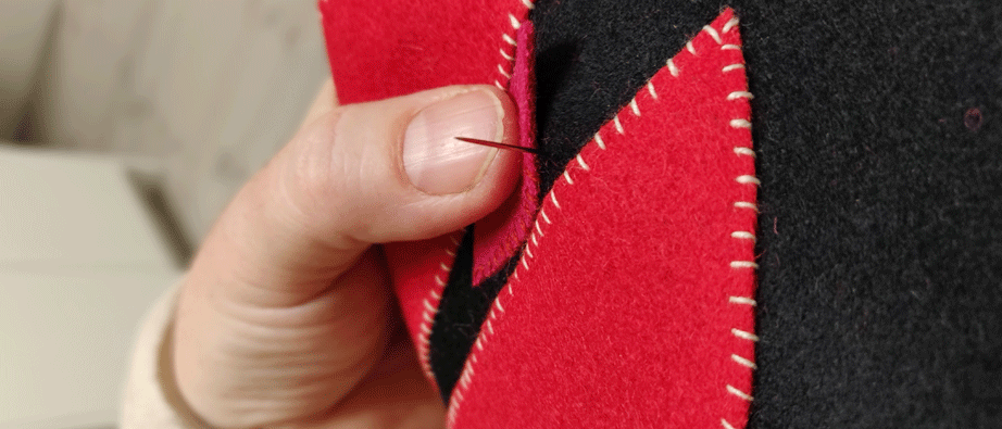 En hand som håller i en nål och syr i rött och svart ylletyg