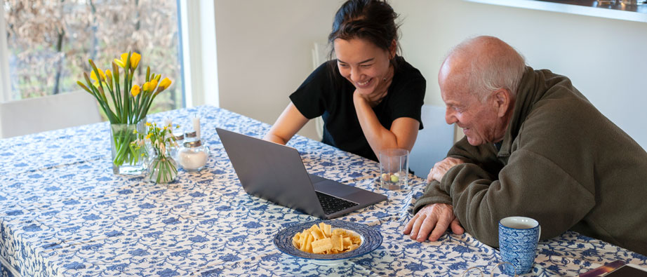 En äldre man som sitter vid ett bord och tittar på en dator tillsammans med en yngre kvinna