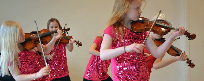 Fyra tjejer spelar fiol och har cerisa glittriga tröjor på sig