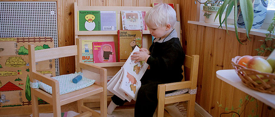 Bild på liten pojke som sitter på en stol i förskolemiljö.
