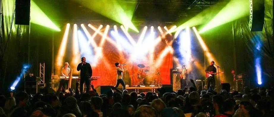 Artister som uppträder på en scen med ett publikhav framför scenen. Massa scenbelysning i rött, blått och grönt.