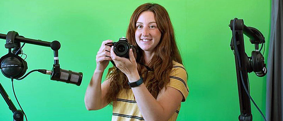 Flicka som håller i kamera inne i studio med grön bakgrund