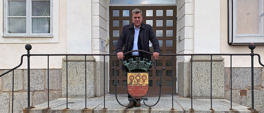 Bild på Anders som står på trappan till Rådhuset med Faluns stadsvapen framför sig,