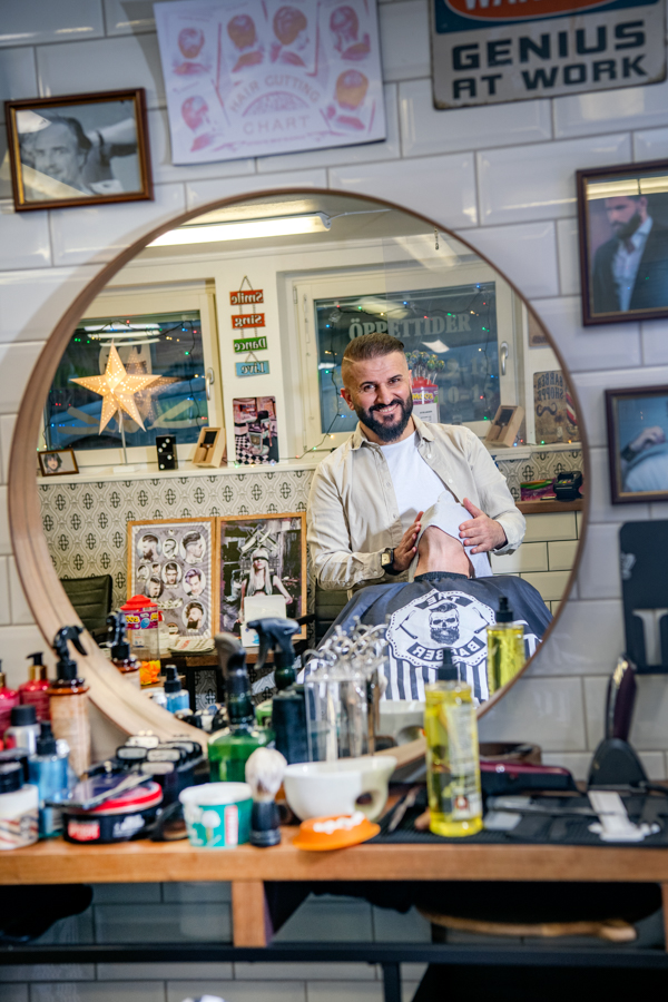 Fotot är taget på Ivans frisörbord och spegel. På bordet ligger ett stort antal hårprodukter. I spegeln syns Ivan när han tar hand om en kund i frisörstolen. 