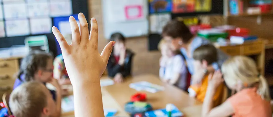 Ett barn som räcker upp handen i ett klassrum med många barn