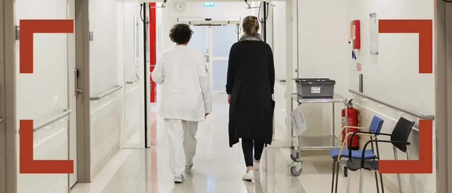 Sjukvårdsmiljö med två personer so går i en korridor, en av dem är sjukvårdspersonal.