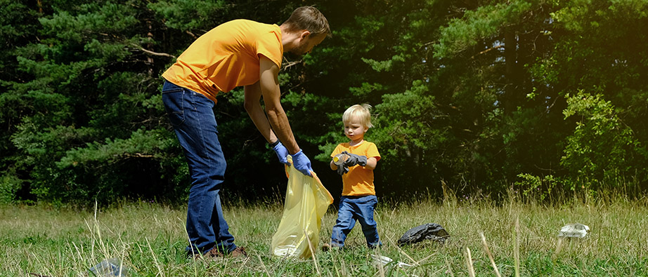Ett litet barn hjälper en vuxen att plocka skräp framför en skogsdunge