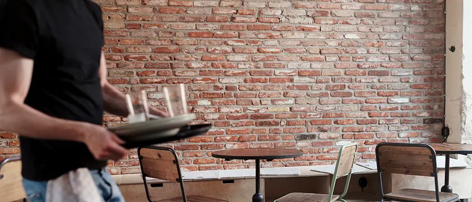 En person som bär på en bricka med två glas på i en restaurang
