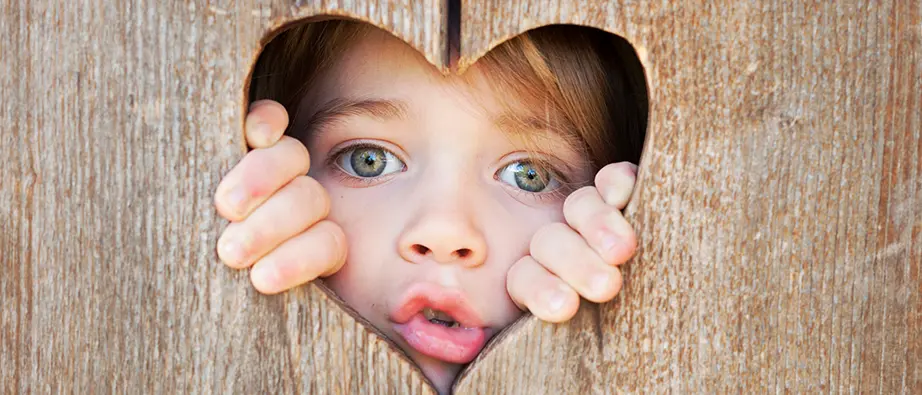 Ett barn som tittar ut ur ett hjärtformat hål på en dörr