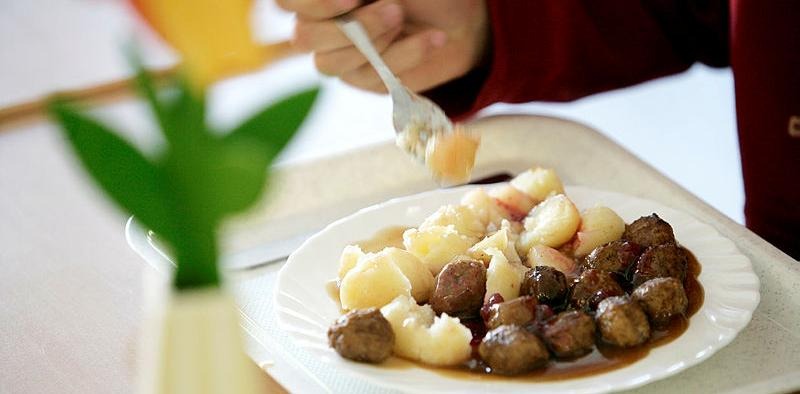 Person äter bricklunch med köttbullar och potatis. Men ser hand med gaffel och tallrik med maten.