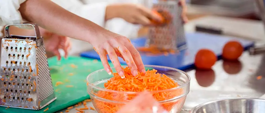 rivna morötter i skål med händer som lägger ner morötterna