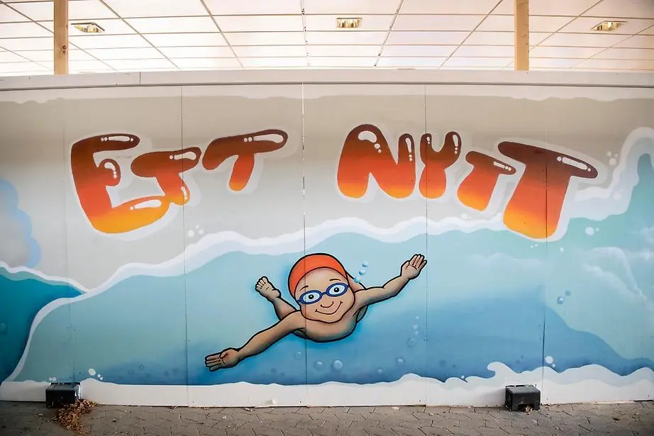 Graffitikonst. Blå bakgrund i olika nyanser för att efterlikna vatten och en person i badmössa som simmar. I text står det "Ett nytt ". 