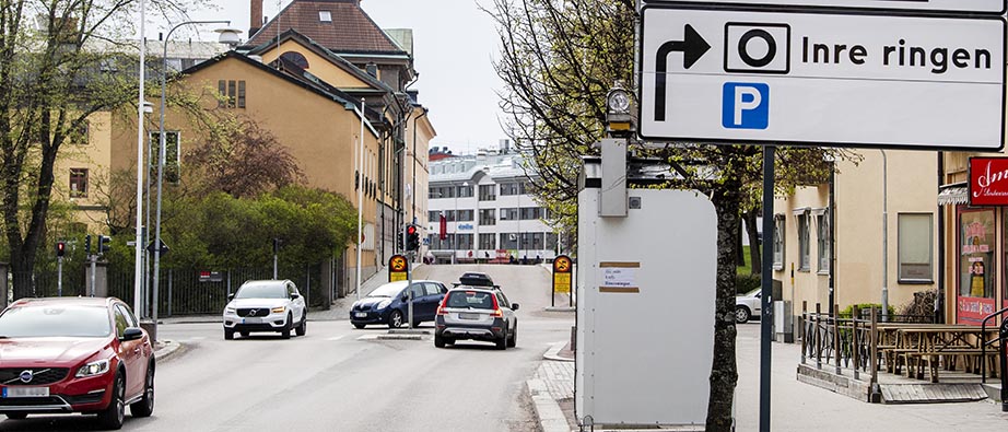 Bilar och stor vit låda vid sidan av gatan som mäter luftkvalitet. Foto Ulf Palm.