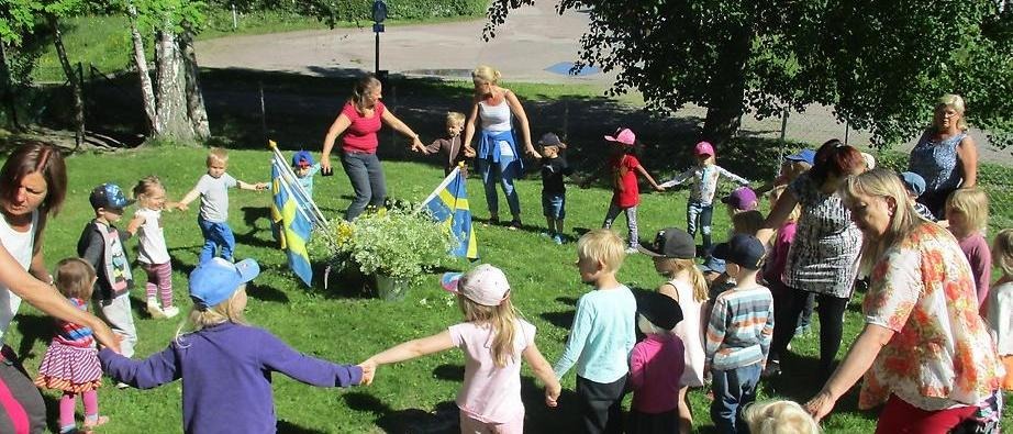 Barn och vuxna som dansar i ring utomhus en sommardag