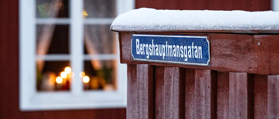 Gatunamnet Berghauptmansgatan sitter på ett rött staket med frost på. I bakgunden lyser en lampa i ett fönster.