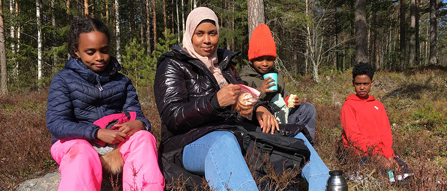 Kvinna och tre barn sitter och fikar i skogen