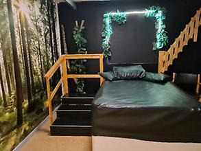 Grönt rum med en stor soffa i mitten och ena väggen har en tapet som ser ut som en skog