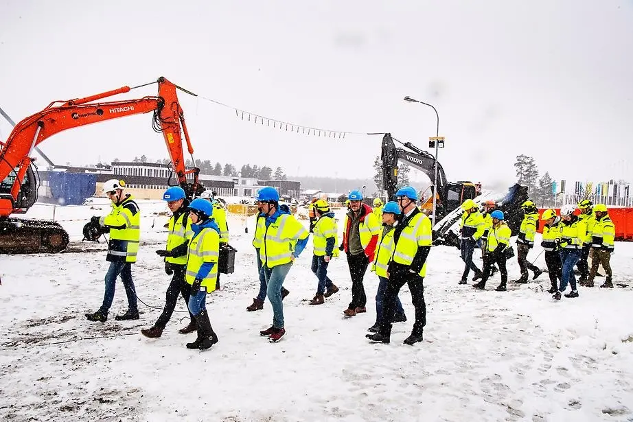 En vintrig marsdag 2020 gick startskottet för bygget av det nya badhuset. På bilden ser man representanter från kommunen, NCC och Lugnet i Falun fanns på plats för att bevittna den historiska dagen. Ett 15 tal personer i gula arbetsjackor går över arbetsplatsen.