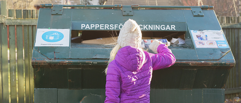 Flicka ses bakifrån stoppa ned något i insamlingscontainer på återvinningsstation