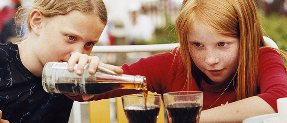 Två barn som häller saft i ett glas.