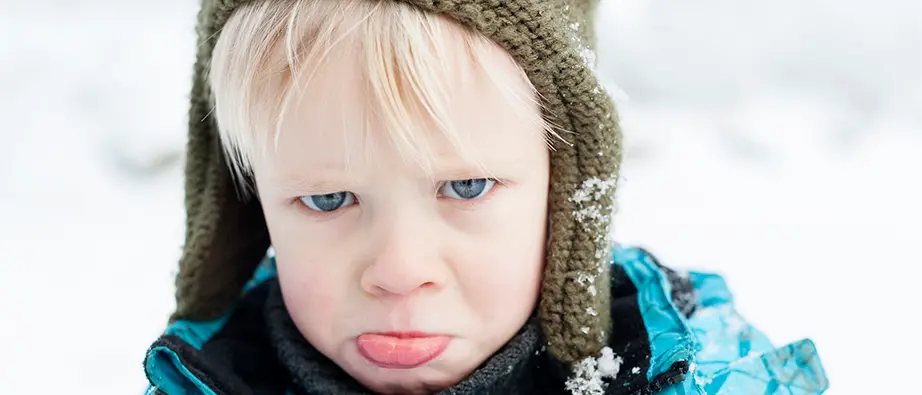 En liten pojke ute i snön som sträcker ut tungan