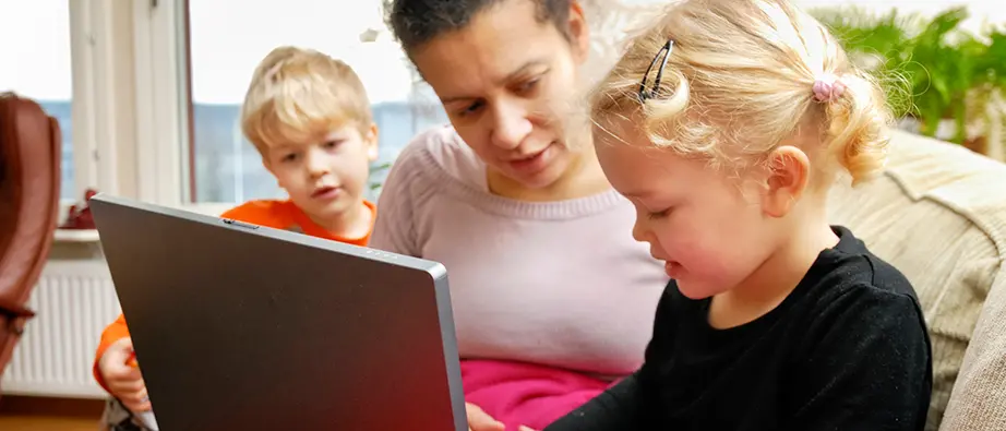 En vuxen och två barn sitter och tittar på en dator i soffan