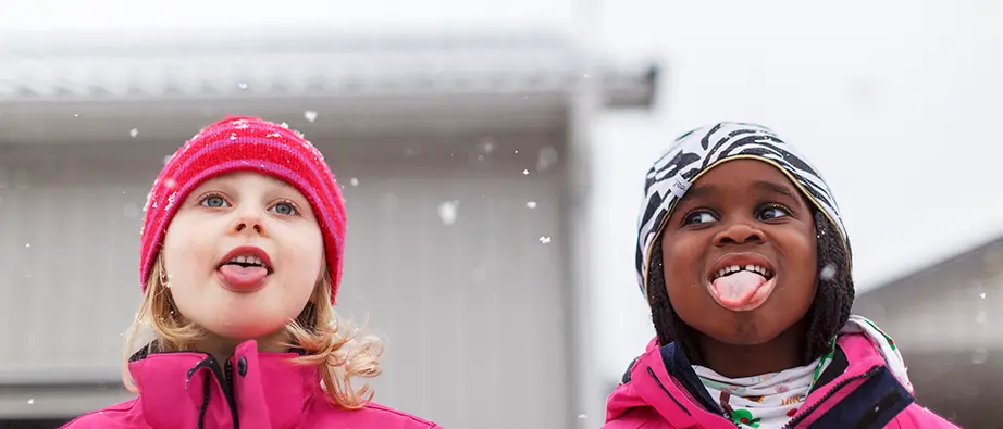 Två barn som står ute när det snöar och båda sträcker ut sina tungor