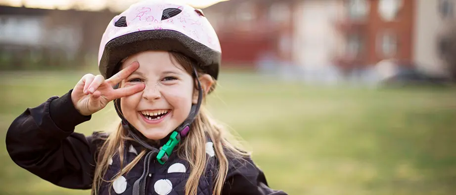 En flicka i cykelhjälm som ler och tittar in i kameran