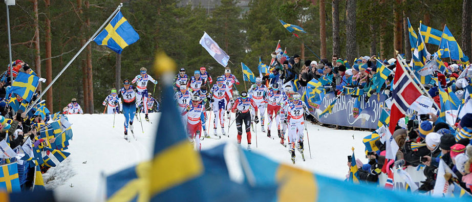Skidåkare i massor åker inför publik som viftar med svenska flaggor