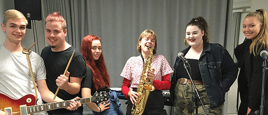Fyra tjejer och två killar står och håller i musikinstrument och ser glada ut